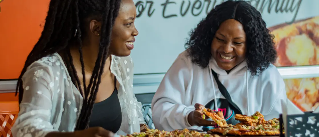 Two friends sharing a meal in a café, laughing over the bill.